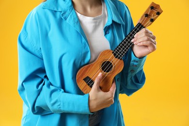 Photo of Woman playing ukulele on orange background, closeup