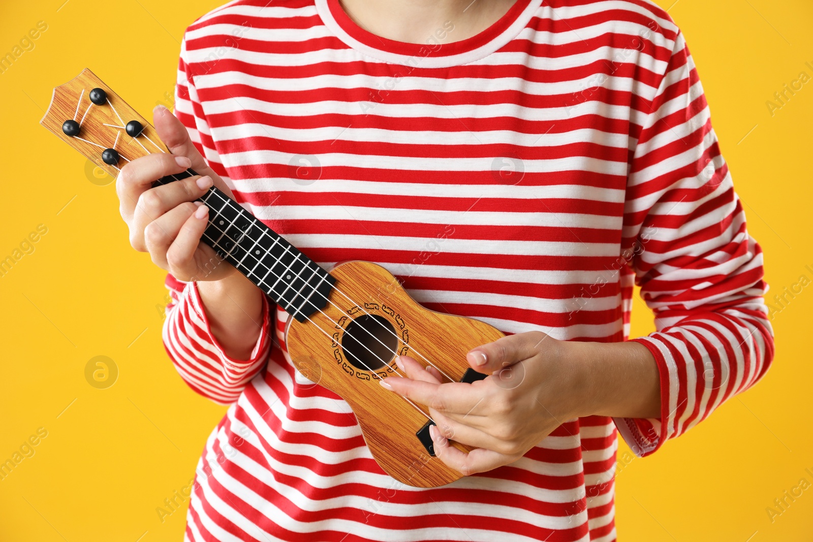 Photo of Woman playing ukulele on orange background, closeup