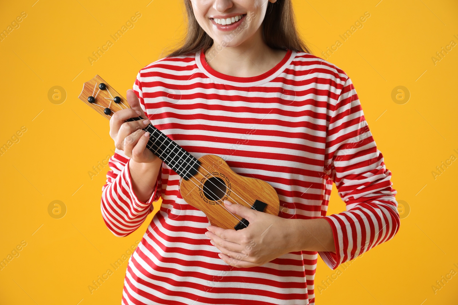 Photo of Woman playing ukulele on orange background, closeup