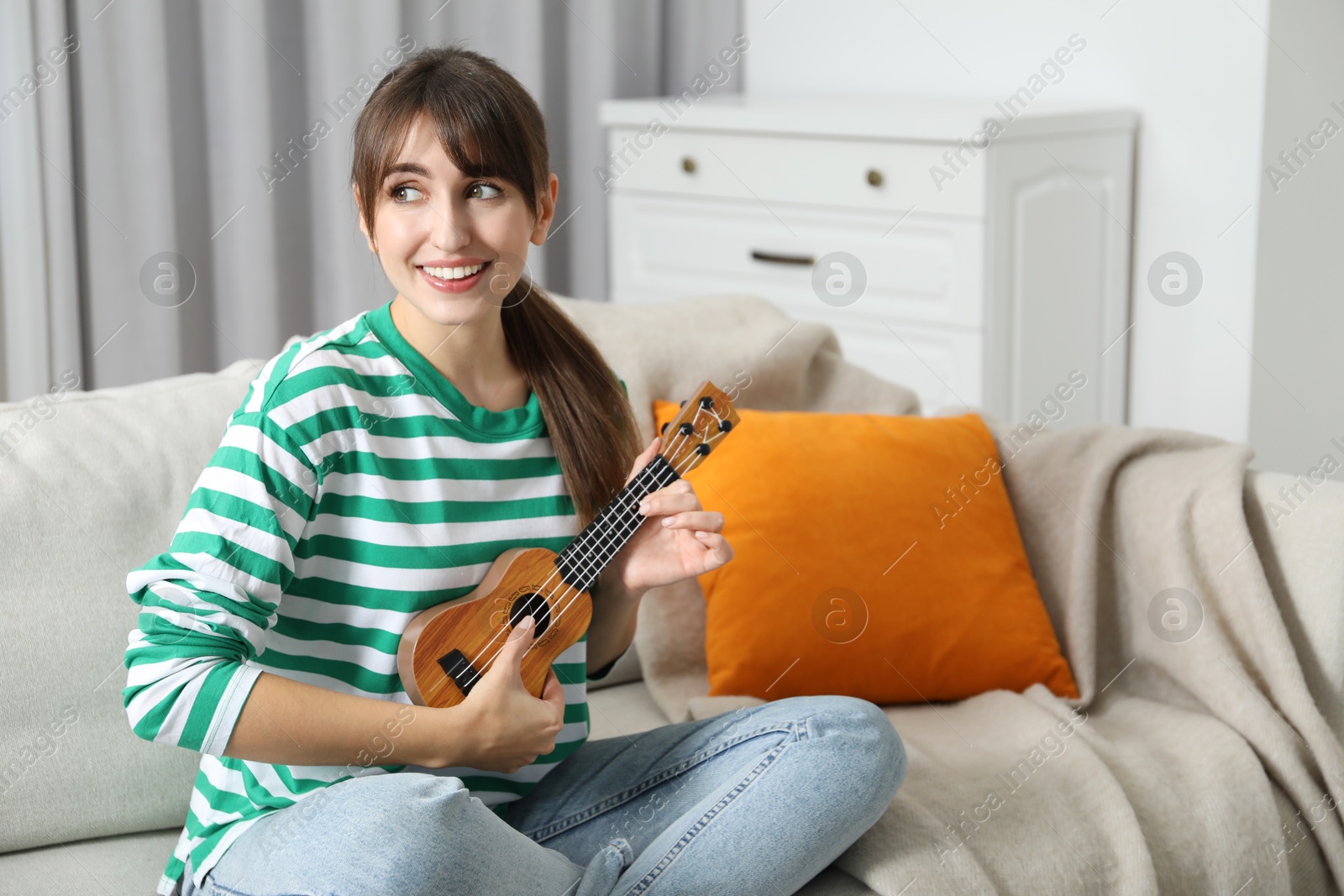 Photo of Happy woman playing ukulele on sofa at home