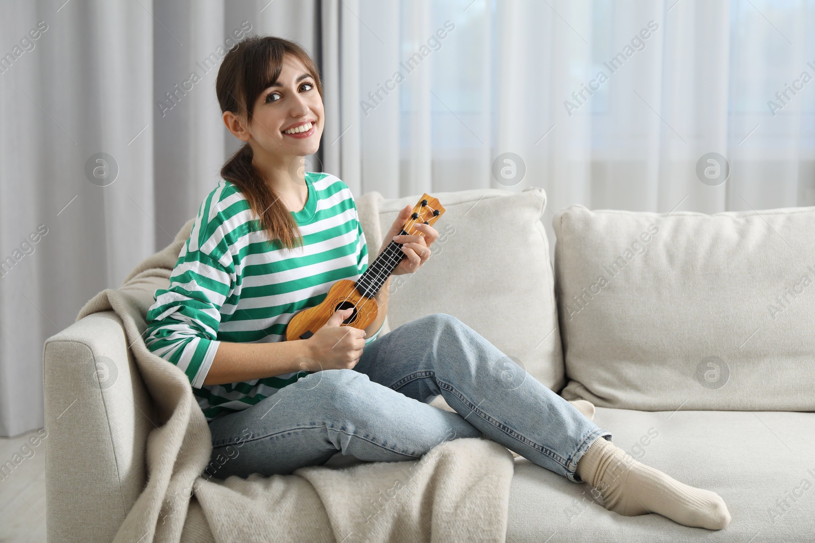 Photo of Happy woman playing ukulele on sofa at home