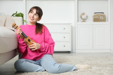 Photo of Happy woman playing ukulele on floor at home, space for text