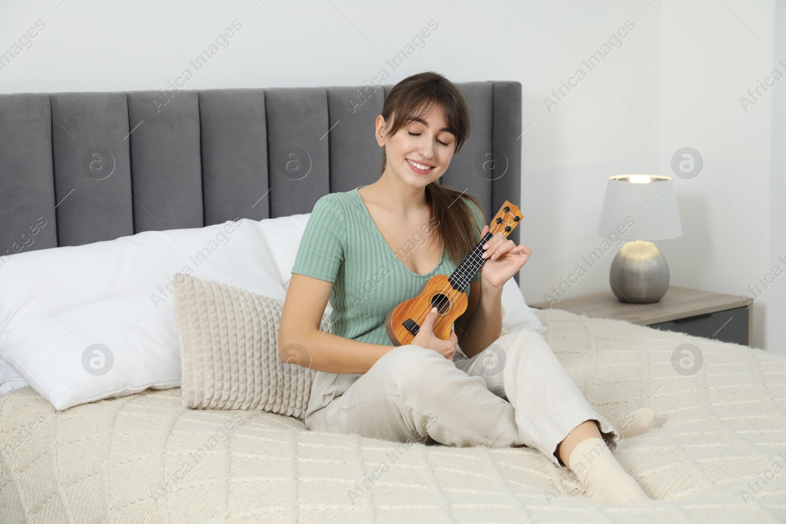 Photo of Happy woman playing ukulele on bed at home