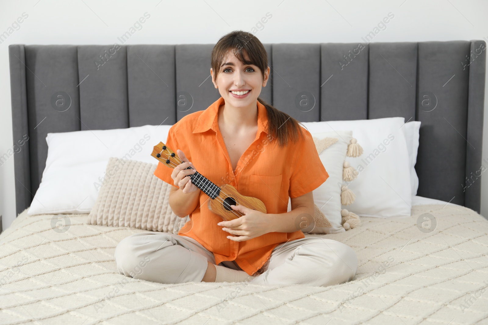 Photo of Happy woman playing ukulele on bed at home