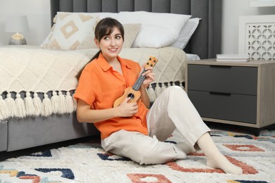 Photo of Happy woman playing ukulele on floor at home