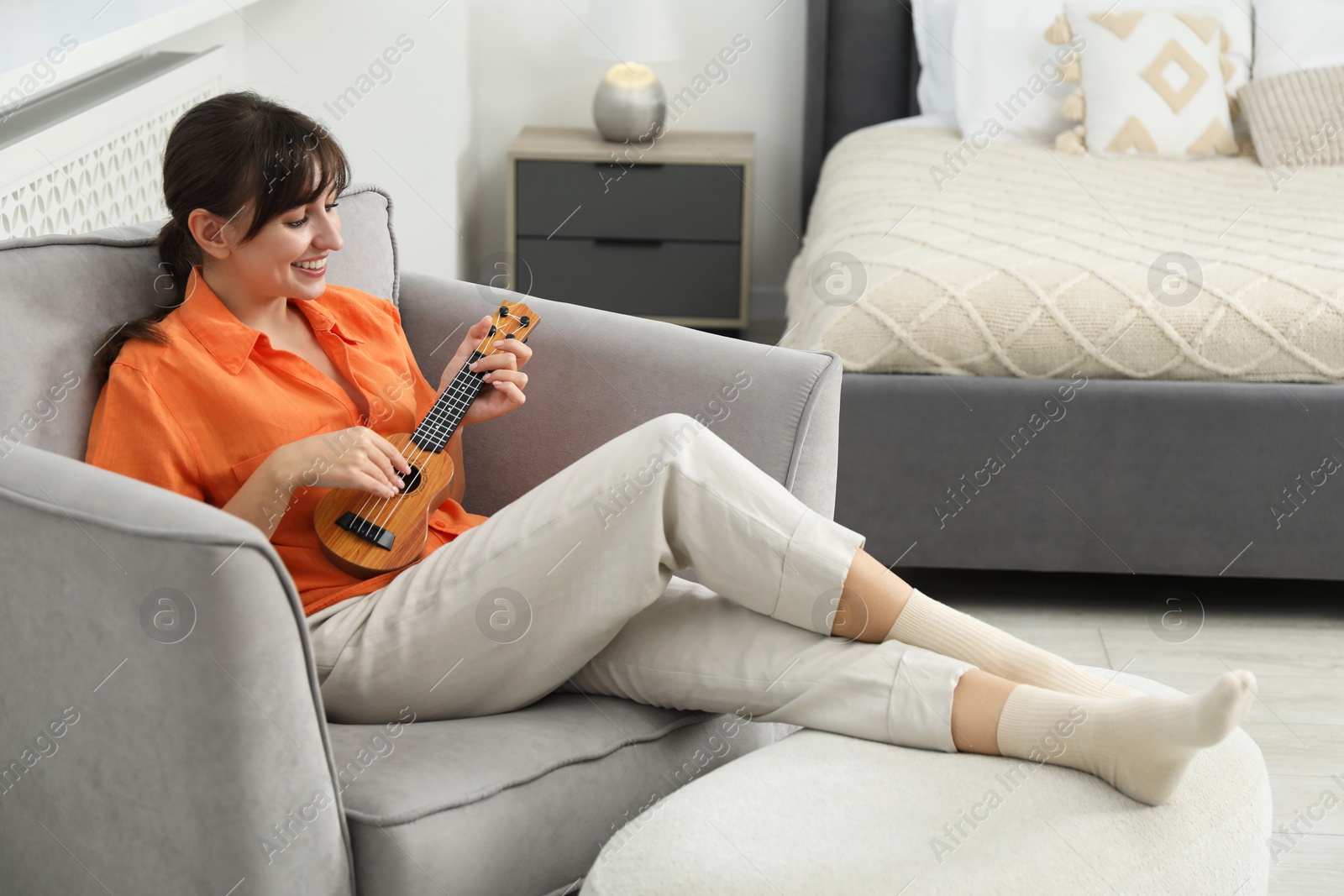 Photo of Happy woman playing ukulele in armchair at home