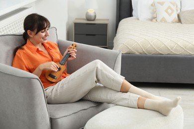 Photo of Happy woman playing ukulele in armchair at home