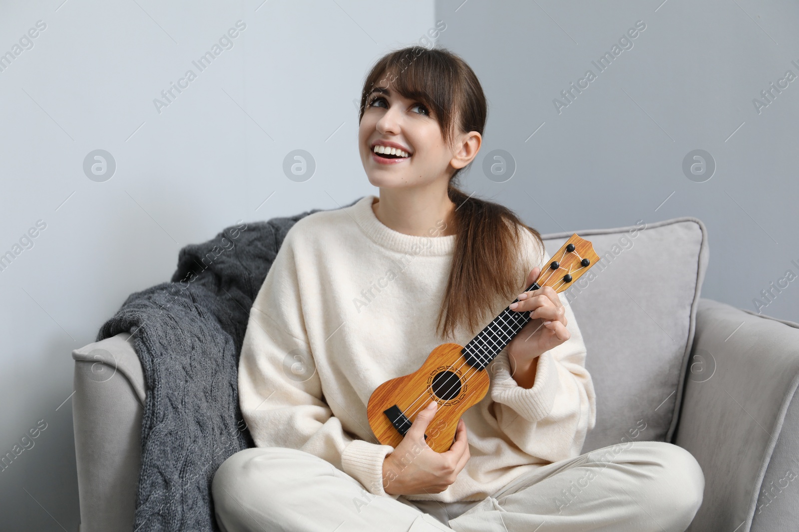 Photo of Happy woman playing ukulele in armchair at home