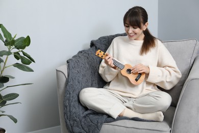 Photo of Happy woman playing ukulele in armchair at home