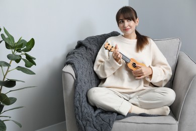 Photo of Happy woman playing ukulele in armchair at home