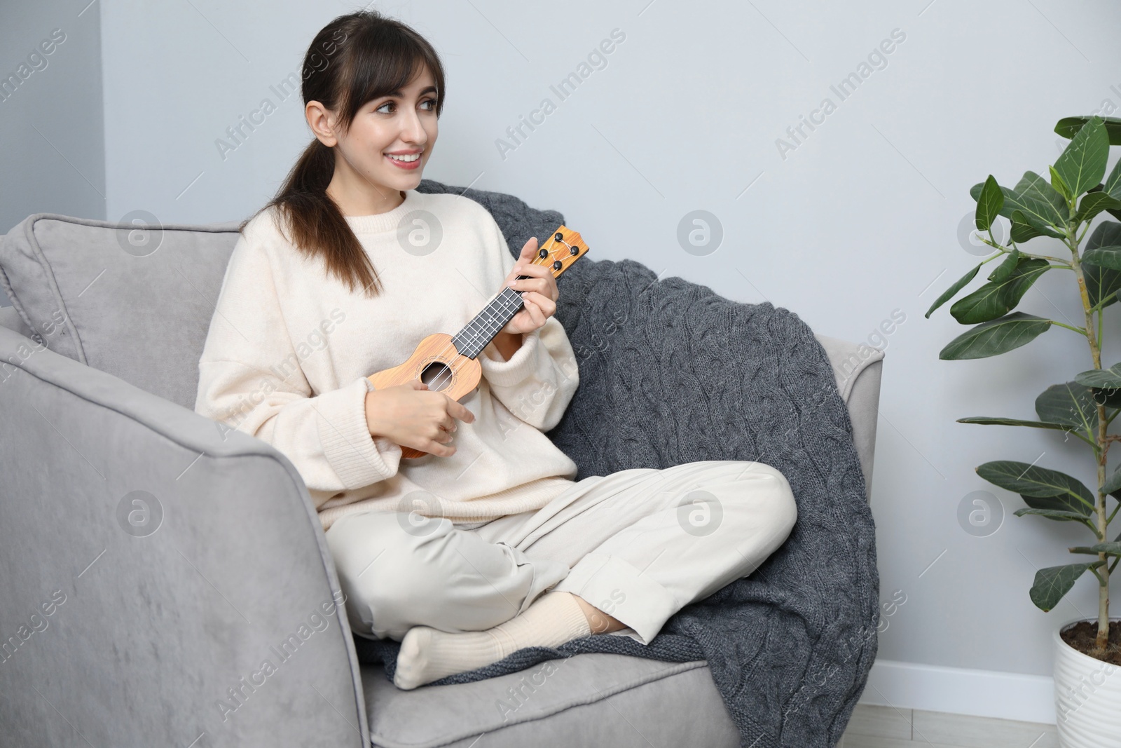 Photo of Happy woman playing ukulele in armchair at home