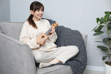 Photo of Happy woman playing ukulele in armchair at home