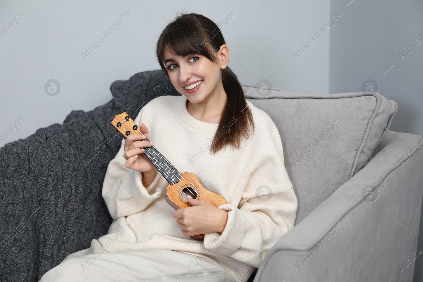 Photo of Happy woman playing ukulele in armchair at home