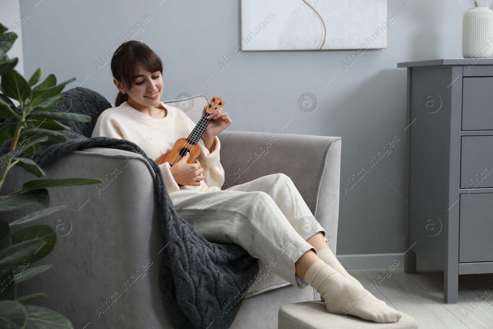 Photo of Happy woman playing ukulele in armchair at home