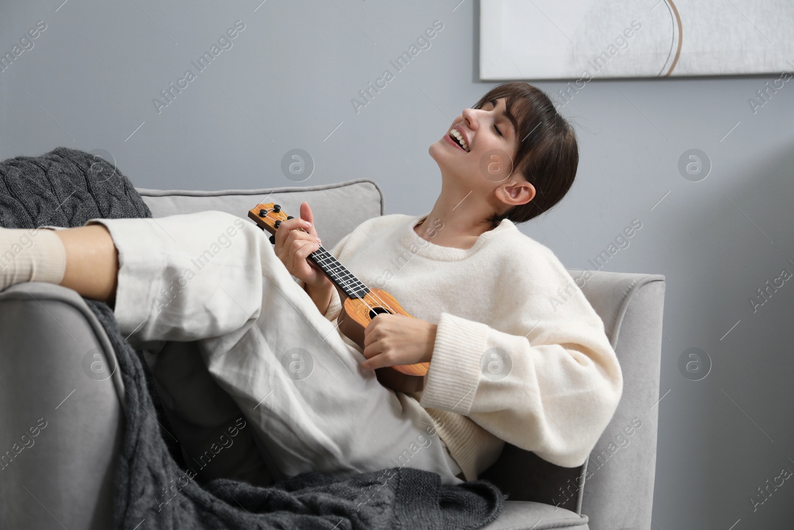 Photo of Happy woman playing ukulele in armchair at home