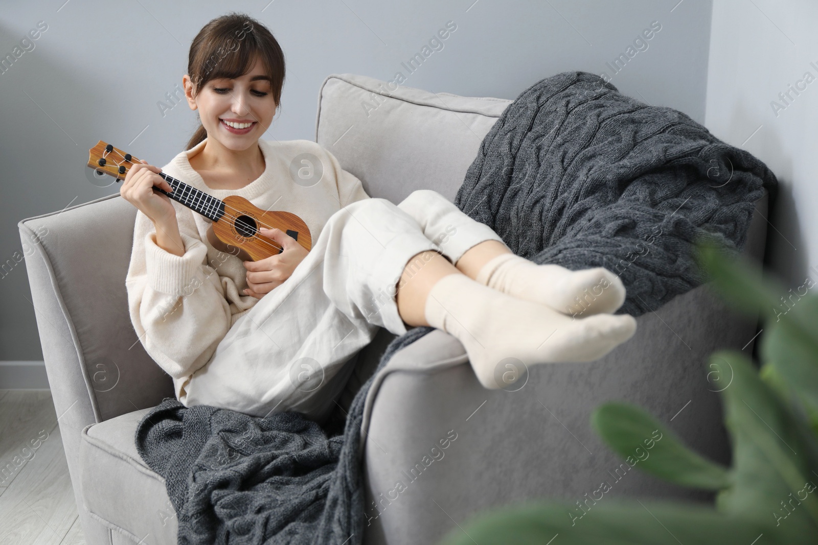 Photo of Happy woman playing ukulele in armchair at home