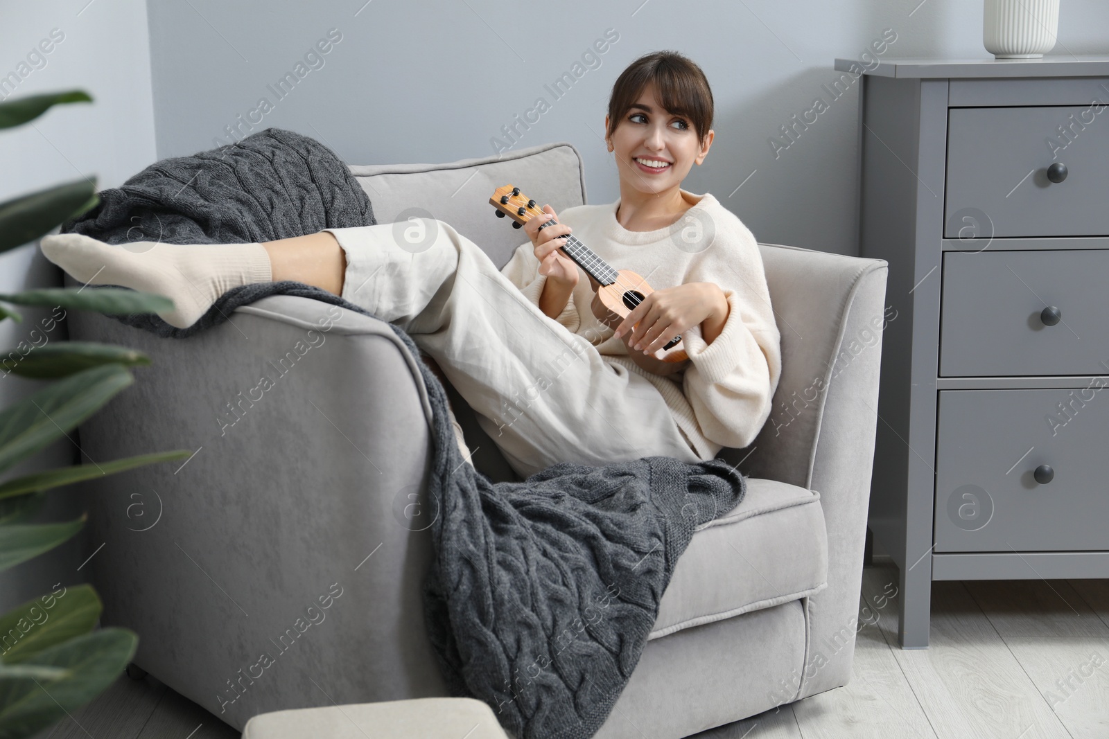 Photo of Happy woman playing ukulele in armchair at home