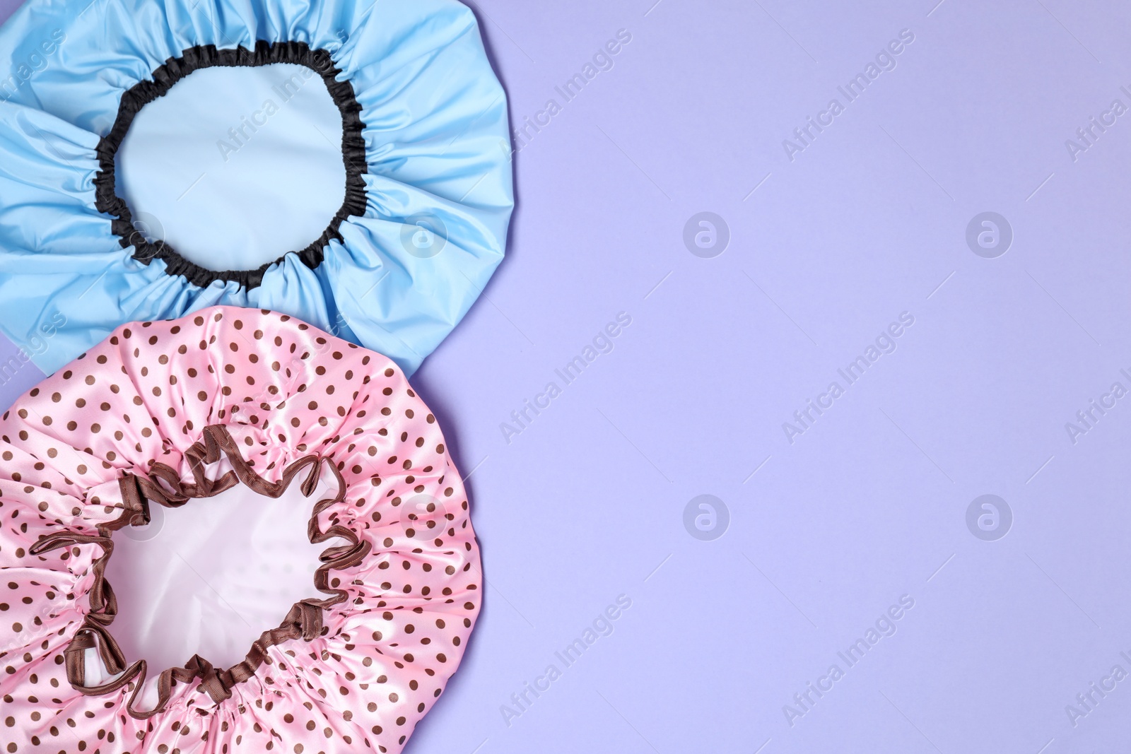 Photo of Two shower caps on lilac background, top view. Space for text