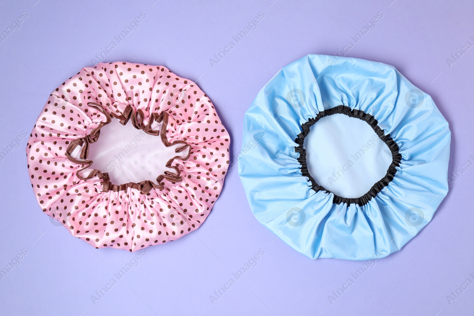 Photo of Two shower caps on lilac background, top view