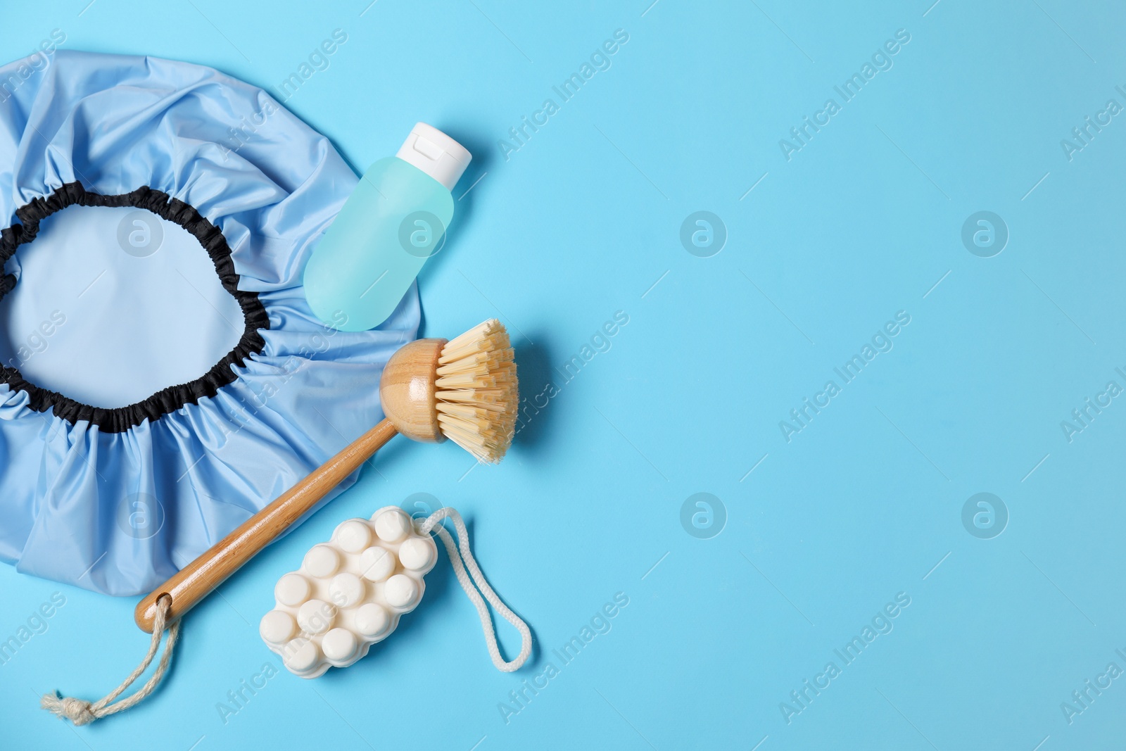 Photo of Shower cap and bath accessories on light blue background, flat lay. Space for text