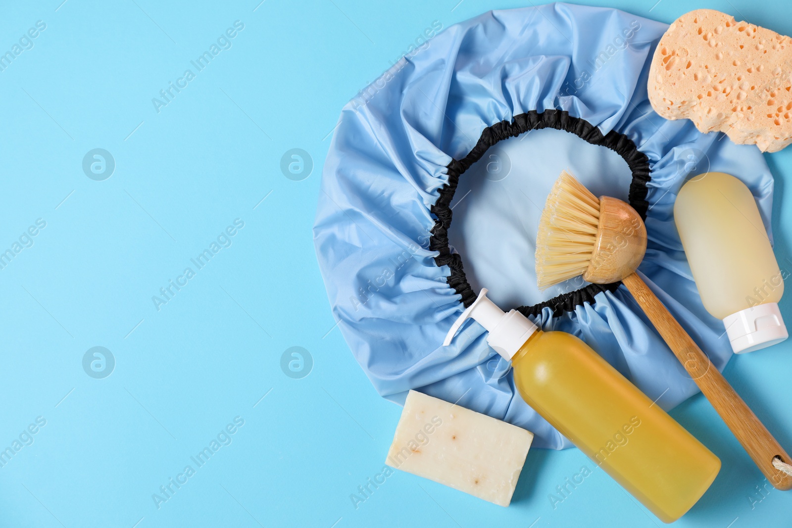 Photo of Shower cap and bath accessories on light blue background, flat lay. Space for text