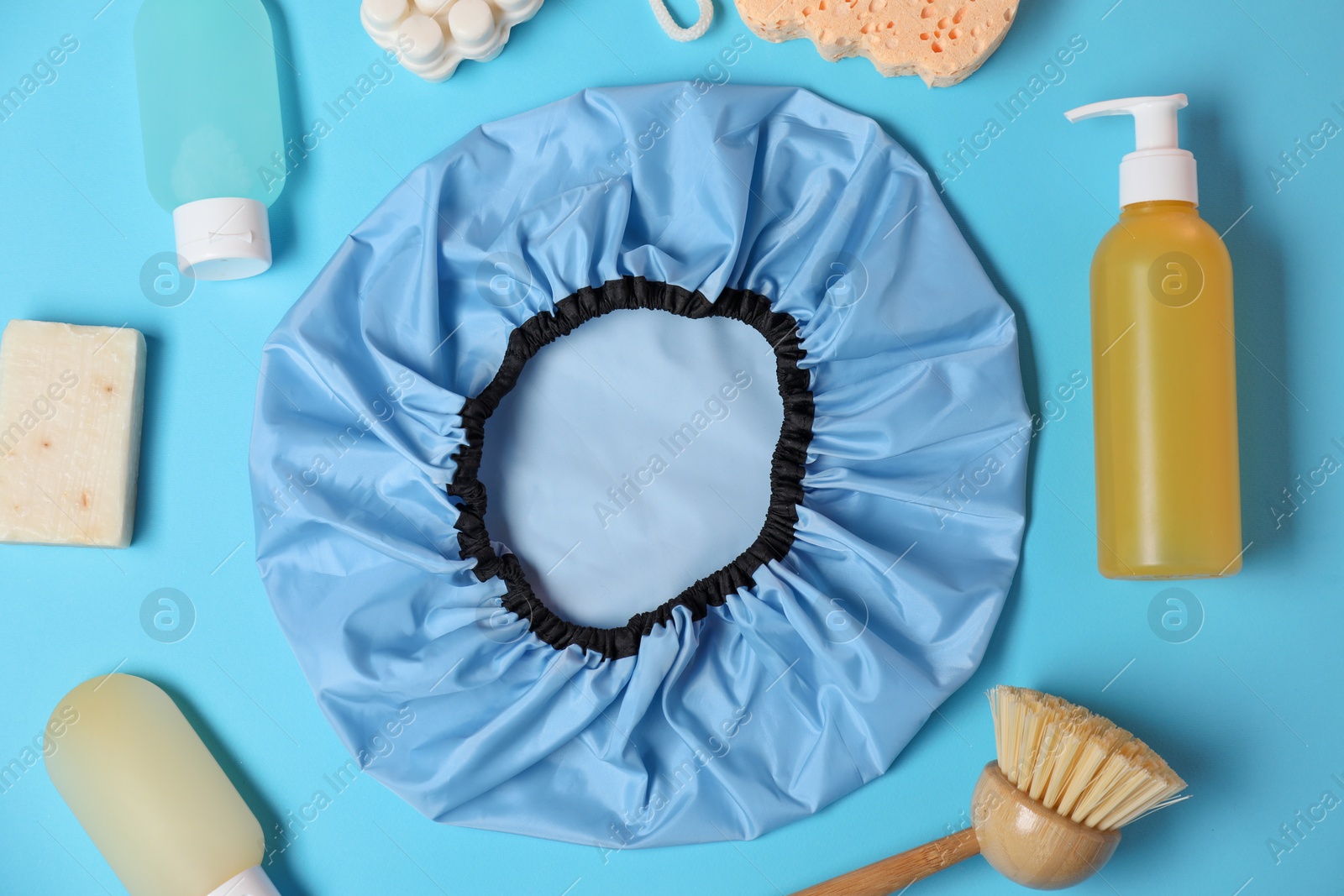 Photo of Shower cap and bath accessories on light blue background, flat lay