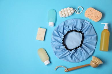 Photo of Shower cap and bath accessories on light blue background, flat lay. Space for text