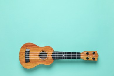 Photo of One ukulele on turquoise background, top view. Space for text