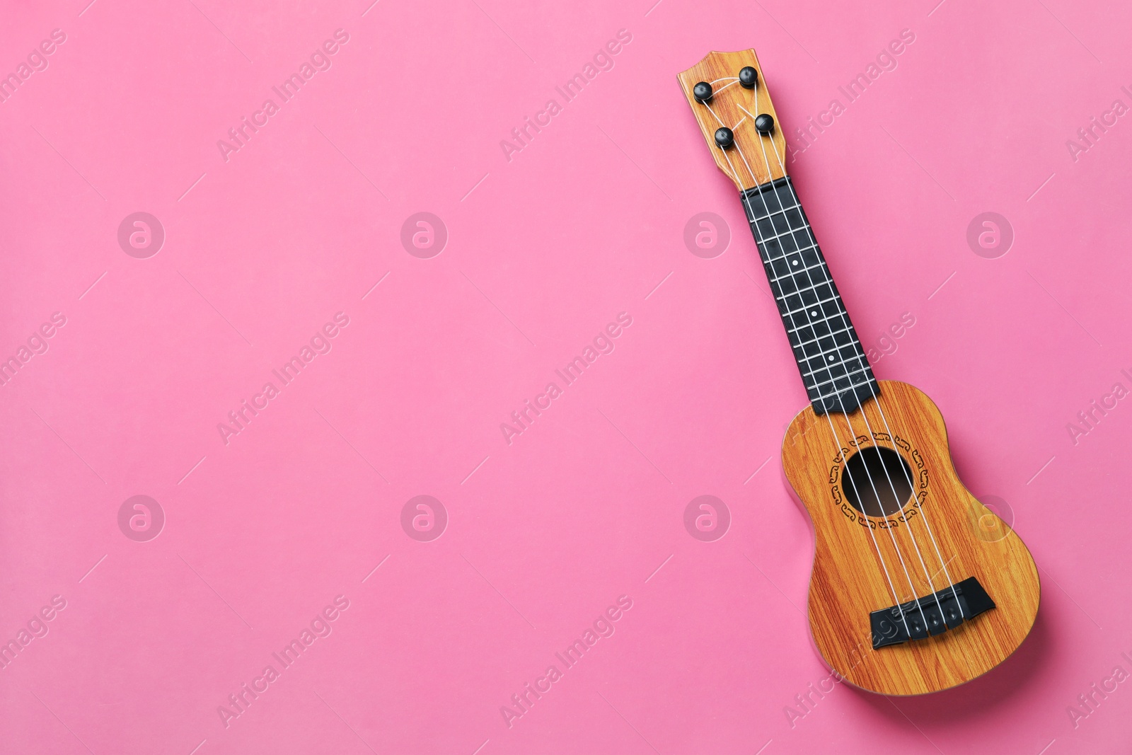 Photo of One ukulele on pink background, top view. Space for text