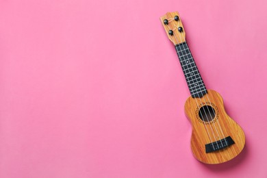 Photo of One ukulele on pink background, top view. Space for text