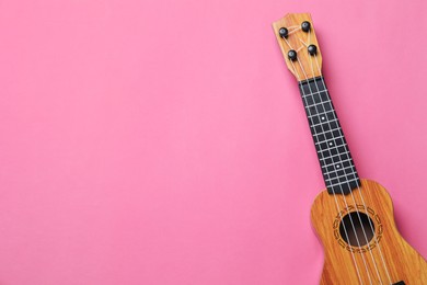 Photo of One ukulele on pink background, top view. Space for text