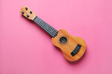 Photo of One ukulele on pink background, top view