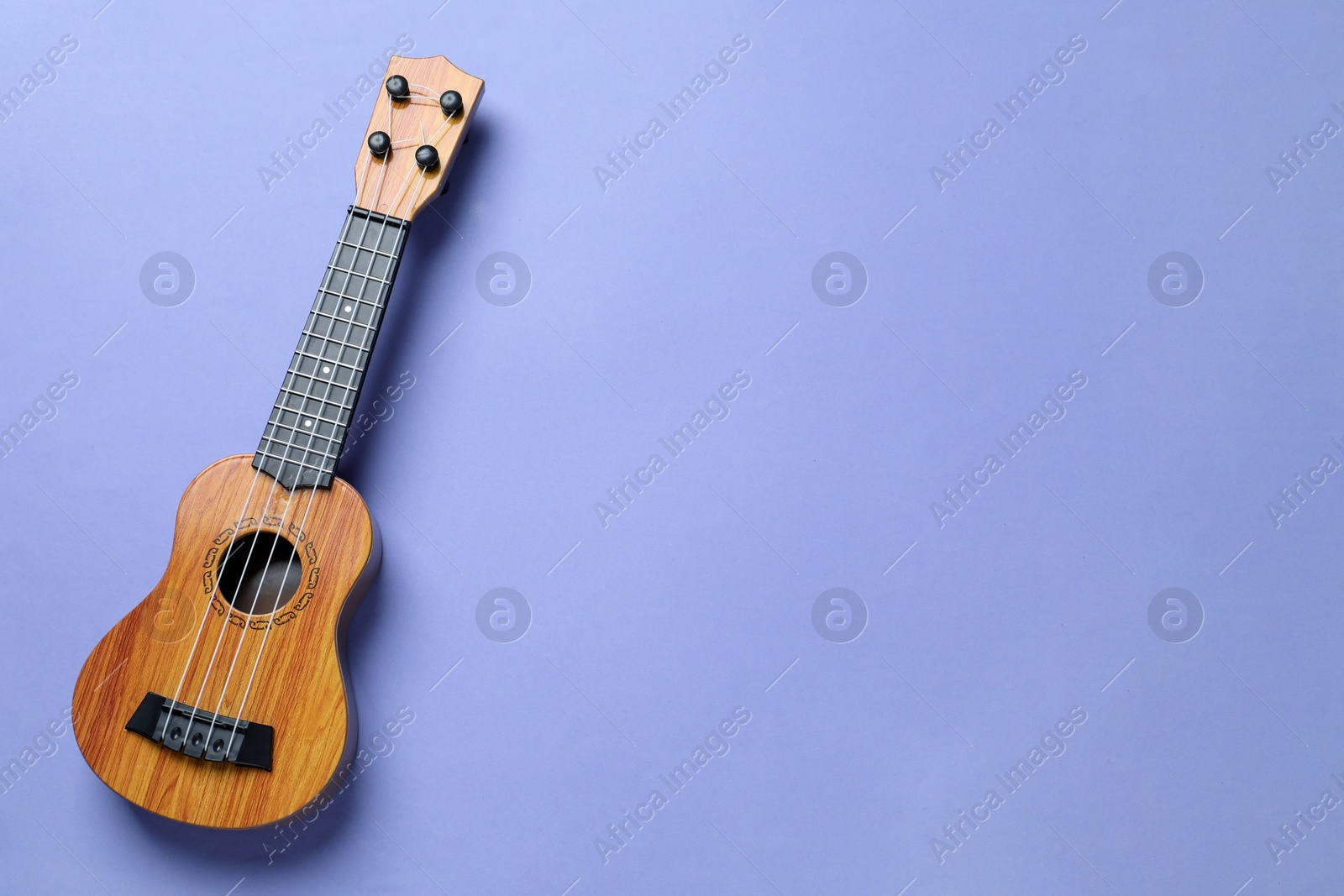 Photo of One ukulele on violet background, top view. Space for text