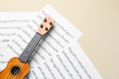 Photo of Ukulele and music sheets on beige background, top view