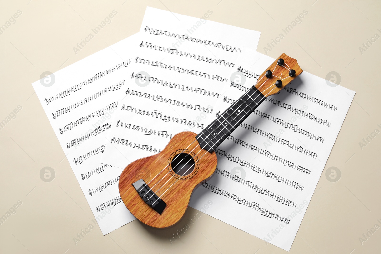 Photo of Ukulele and music sheets on beige background, top view