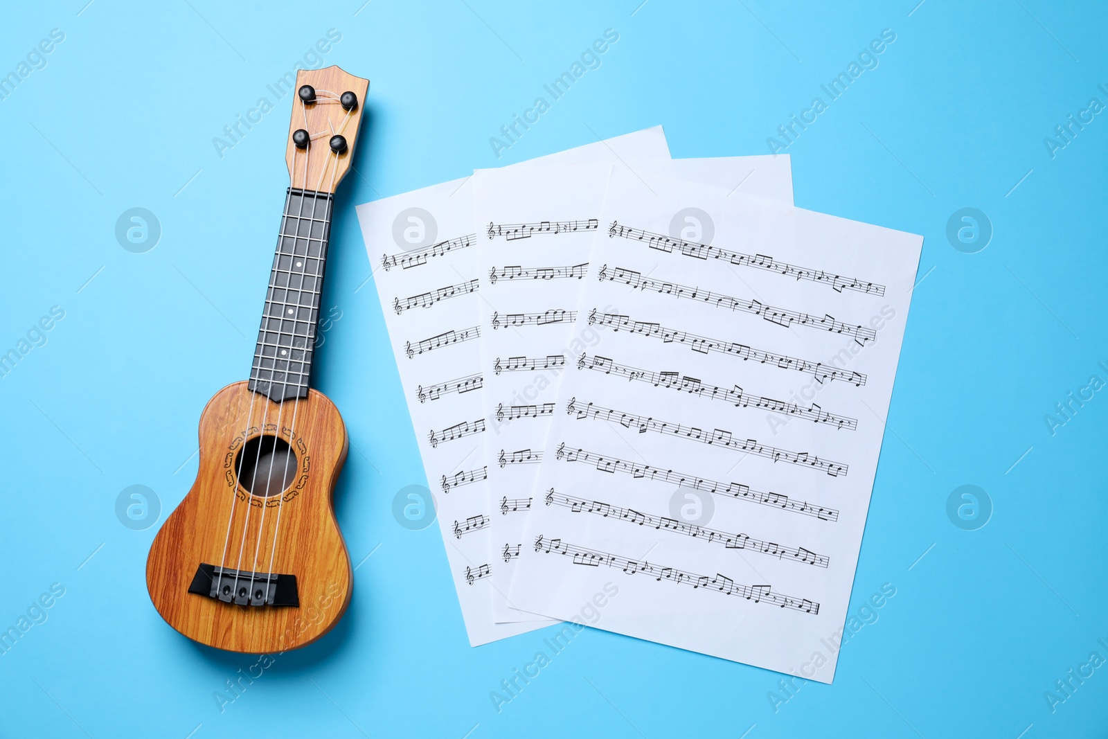 Photo of Ukulele and music sheets on light blue background, top view