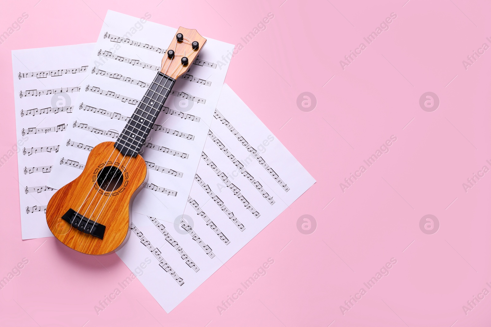 Photo of Ukulele and music sheets on pink background, top view. Space for text