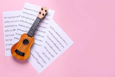 Photo of Ukulele and music sheets on pink background, top view. Space for text