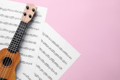 Photo of Ukulele and music sheets on pink background, top view. Space for text