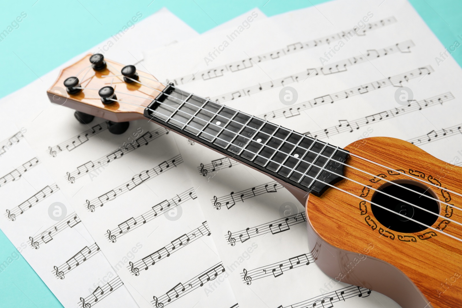 Photo of Ukulele and music sheets on turquoise background, closeup