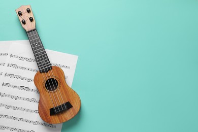 Photo of Ukulele and music sheets on turquoise background, top view. Space for text