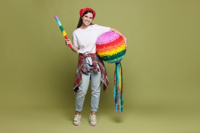 Photo of Happy woman with colorful pinata and stick on green background