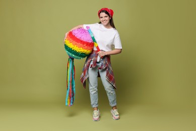 Happy woman with colorful pinata and stick on green background