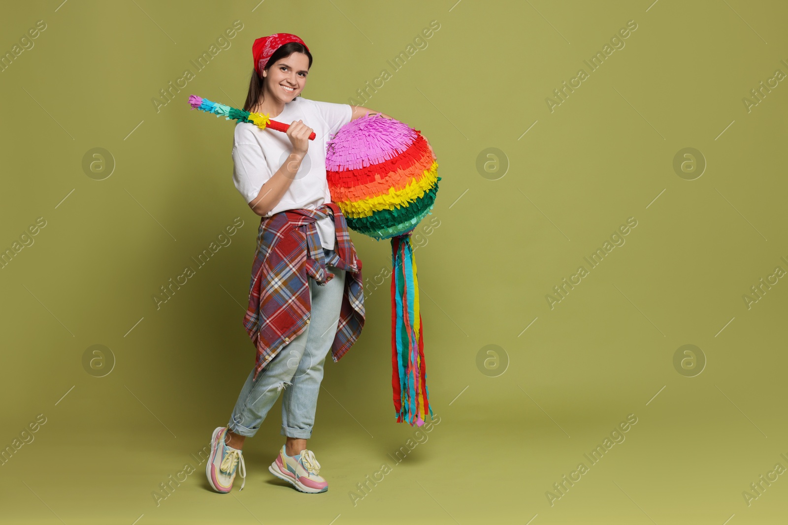 Photo of Happy woman with colorful pinata and stick on green background, space for text