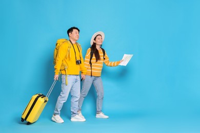 Photo of Happy travellers with suitcase and map on light blue background