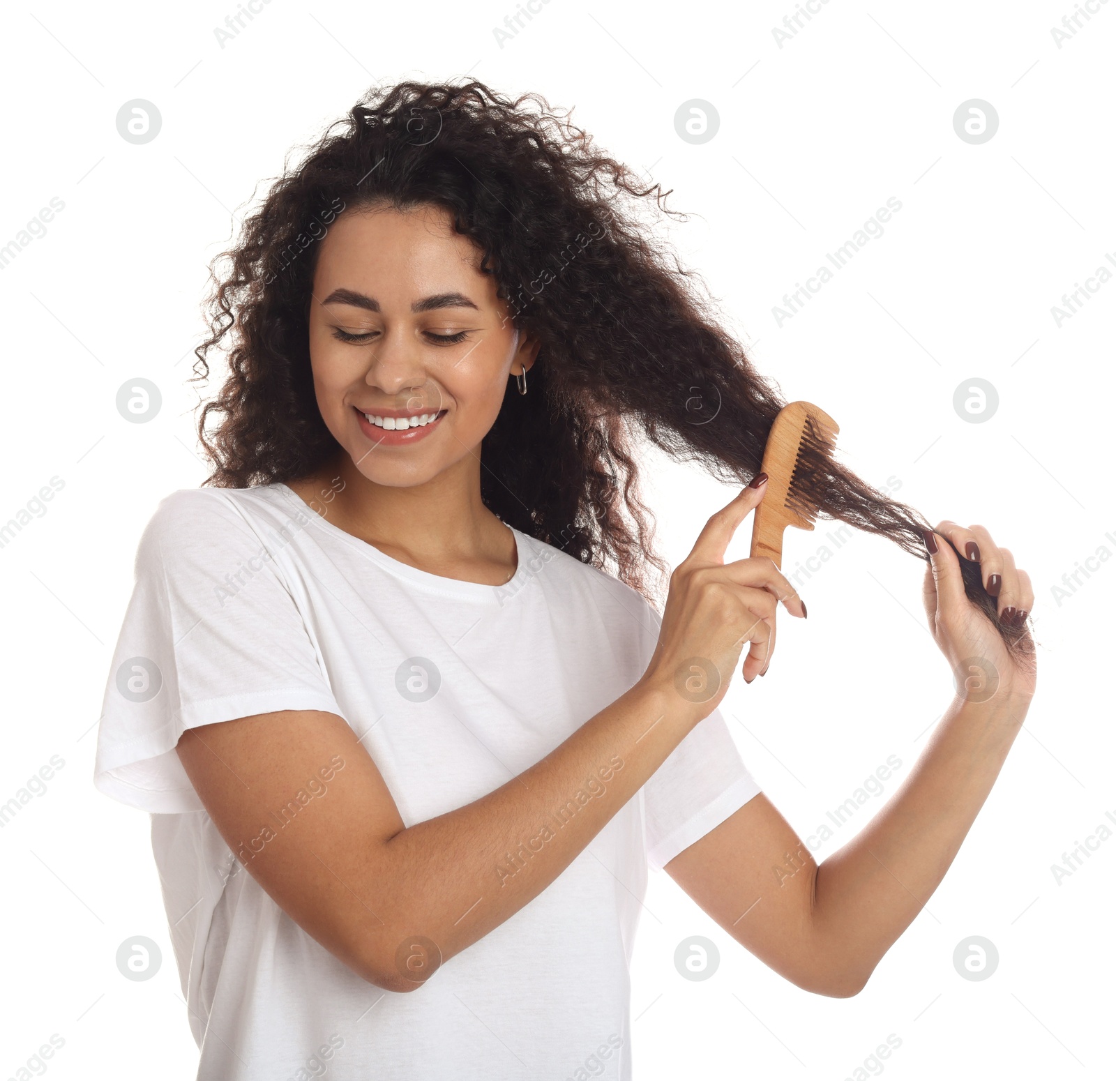 Photo of Smiling young woman brushing her curly hair with comb on white background