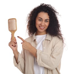 Photo of Smiling young woman with curly hair pointing at wooden brush on white background