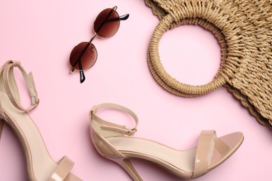 Photo of Wicker bag, heels and sunglasses on light pink background, flat lay. Stylish accessories