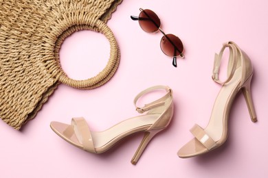 Photo of Wicker bag, heels and sunglasses on light pink background, flat lay. Stylish accessories