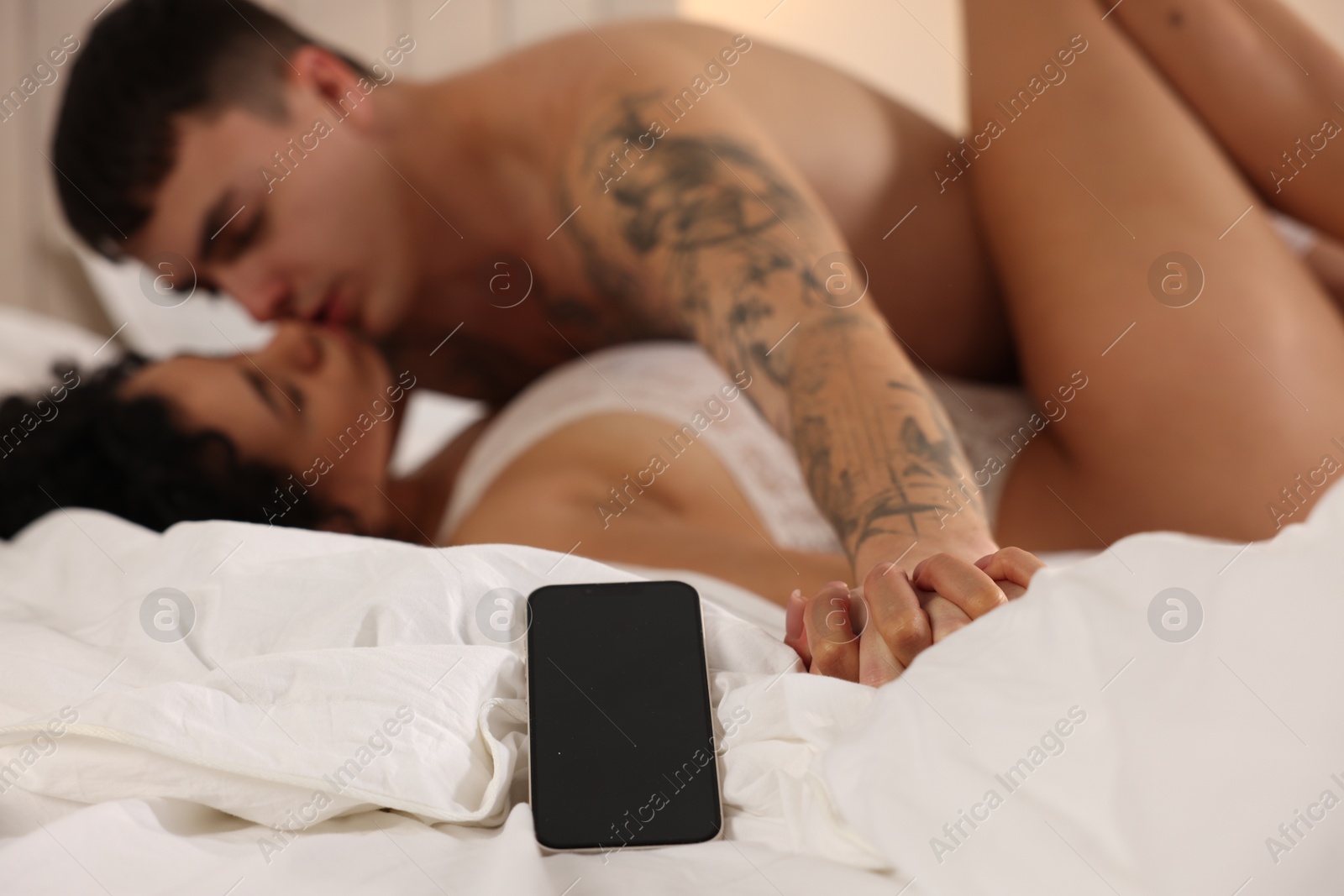 Photo of Betrayal. Passionate lovers having sex on bed, focus on smartphone